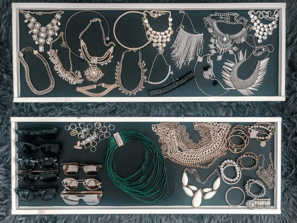 chunky necklaces, sunglesses, and other jewelry organized neatly in ikea komplement trays for organizing jewelry in your closet